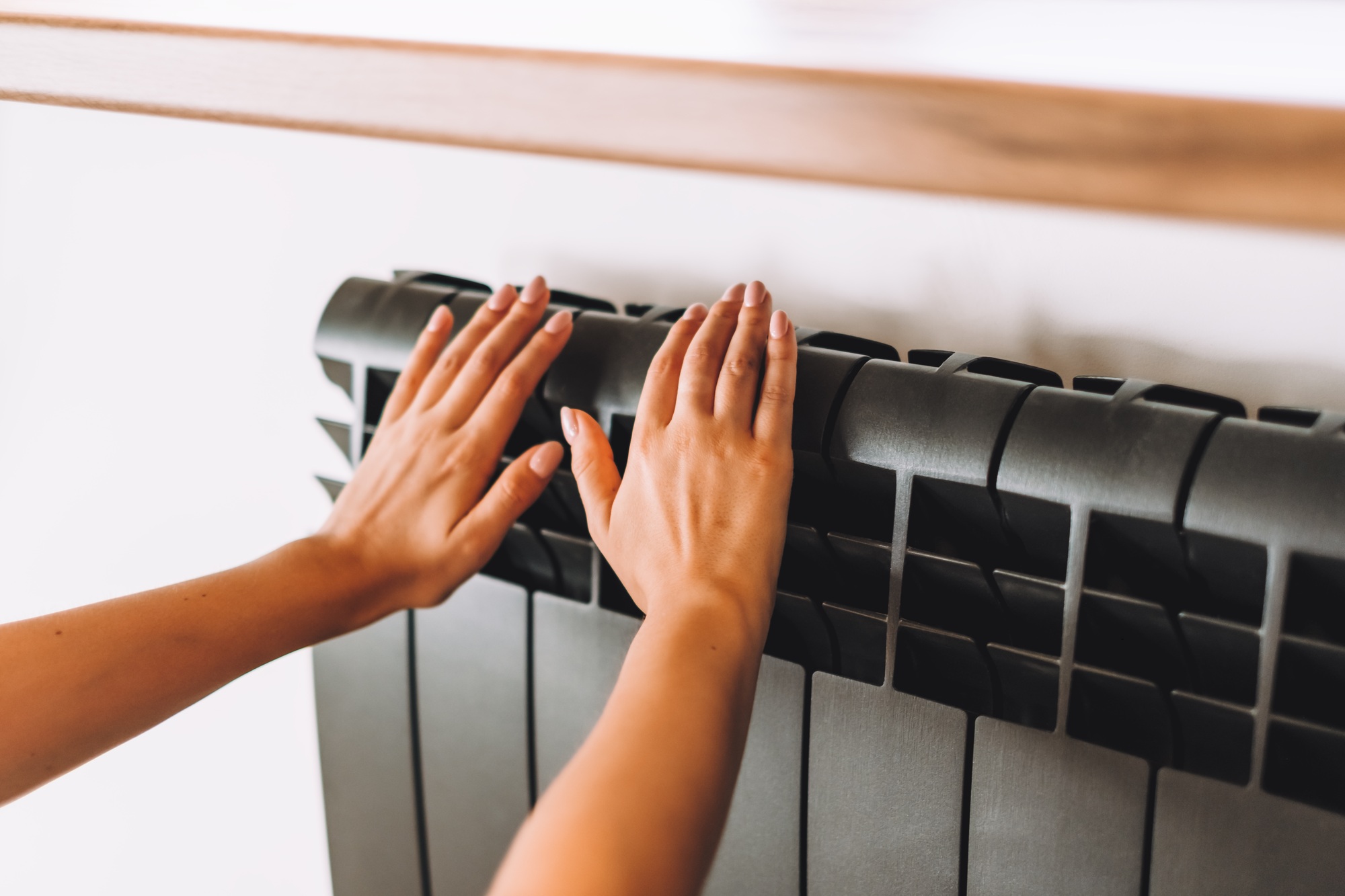Woman warms up hands over heater. Concept of the need for good central heating.